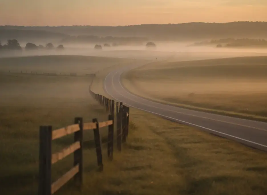 A two-lane country highway through misty Virginia farmland at dawn